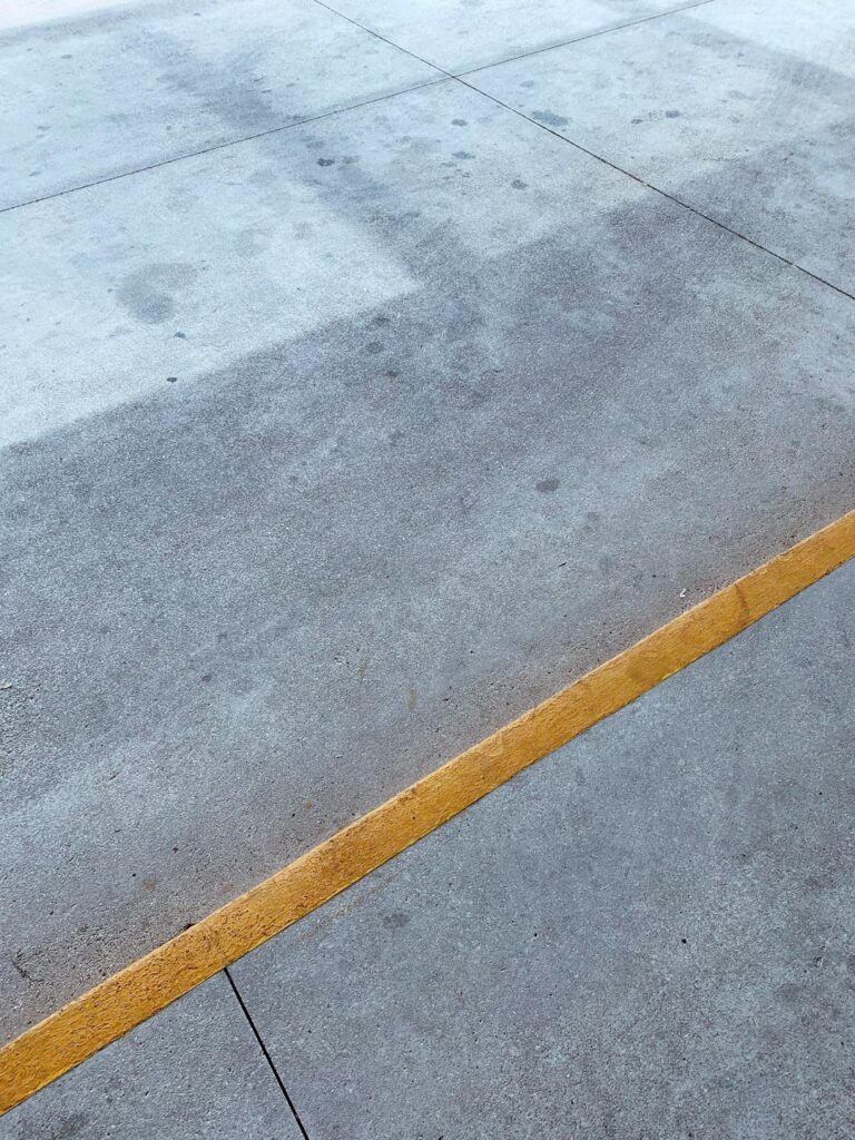 A close view of a residential concrete driveway showing cracks and surface discoloration.