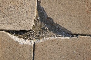 A close-up of cracked, weathered concrete pavement with visible spalling and surface flaking.