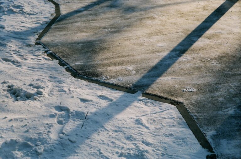 Shovel and ice melt granules scattered on a concrete driveway with patches of snow and exposed pavement.