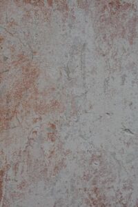 Person scrubbing a dark oil stain from a concrete driveway with a stiff brush and cleaning solution.